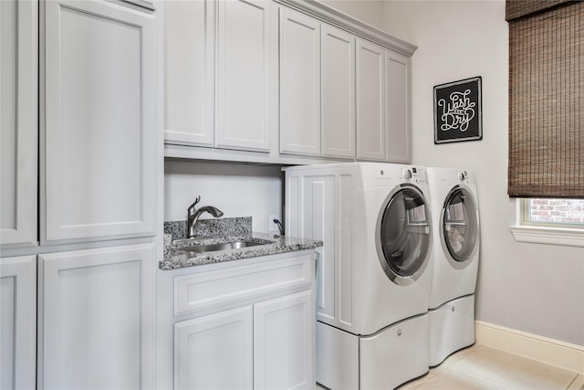 laundry area featuring washing machine and dryer, a sink, baseboards, cabinet space, and tile patterned floors