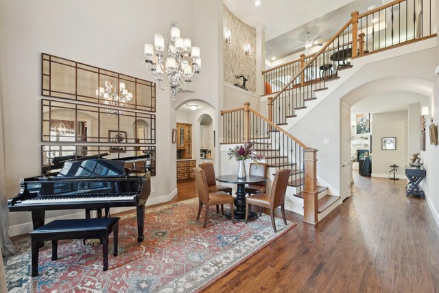 living room featuring arched walkways, wood finished floors, a towering ceiling, baseboards, and stairs