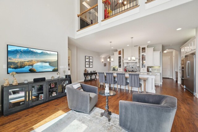 kitchen with dark wood finished floors, decorative backsplash, an island with sink, built in appliances, and a notable chandelier