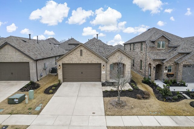 french provincial home featuring brick siding, roof with shingles, central air condition unit, concrete driveway, and a garage