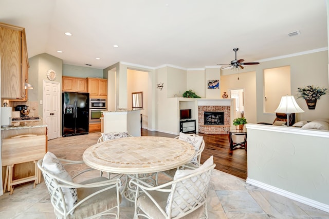 dining area with visible vents, crown molding, a brick fireplace, ceiling fan, and vaulted ceiling