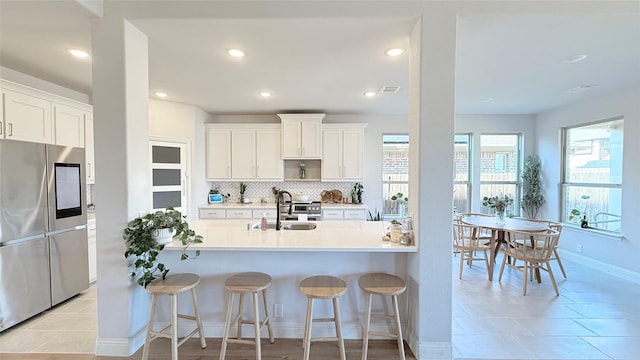 kitchen with decorative backsplash, smart refrigerator, white cabinetry, a sink, and a kitchen breakfast bar