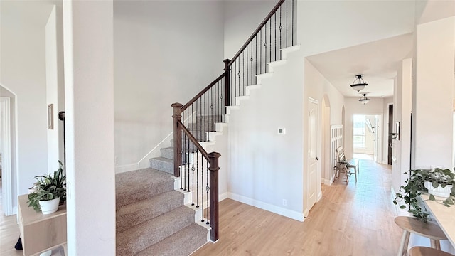 stairs featuring a towering ceiling, baseboards, and wood finished floors