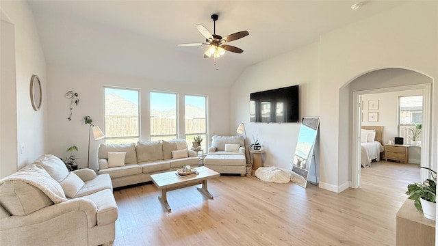 living room with a healthy amount of sunlight, light wood-style floors, arched walkways, and vaulted ceiling