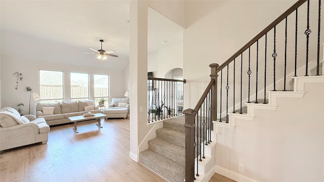 living room with baseboards, a ceiling fan, a towering ceiling, stairway, and wood finished floors