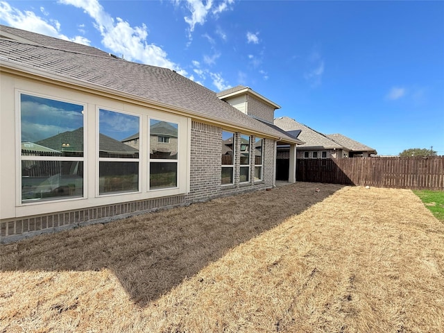 rear view of house with a shingled roof, a yard, brick siding, and fence