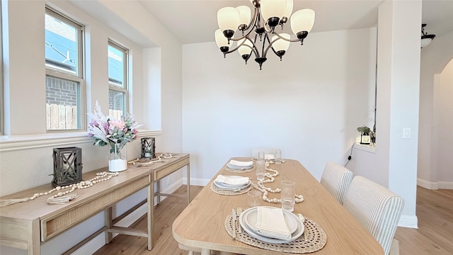 dining room with baseboards, light wood finished floors, arched walkways, and an inviting chandelier