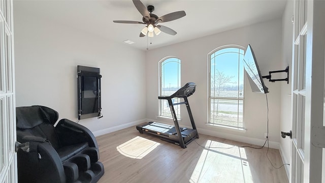 exercise room with light wood-style floors, ceiling fan, and baseboards