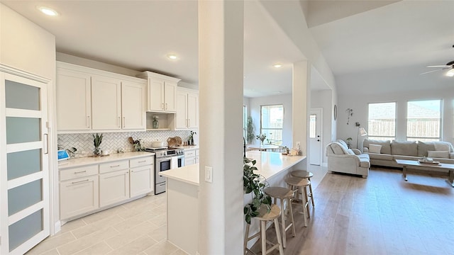 kitchen with a breakfast bar area, backsplash, open floor plan, white cabinets, and stainless steel range with electric stovetop