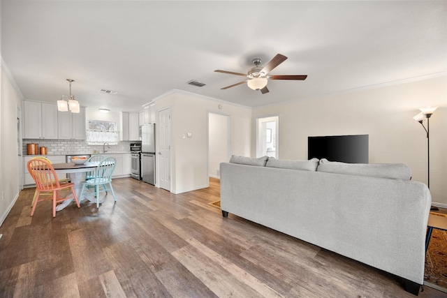 living room featuring ceiling fan, visible vents, wood finished floors, and ornamental molding