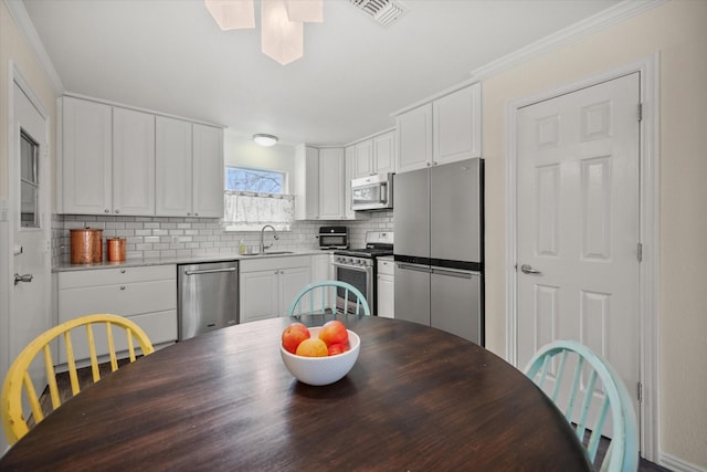 kitchen featuring tasteful backsplash, visible vents, white cabinets, stainless steel appliances, and a sink