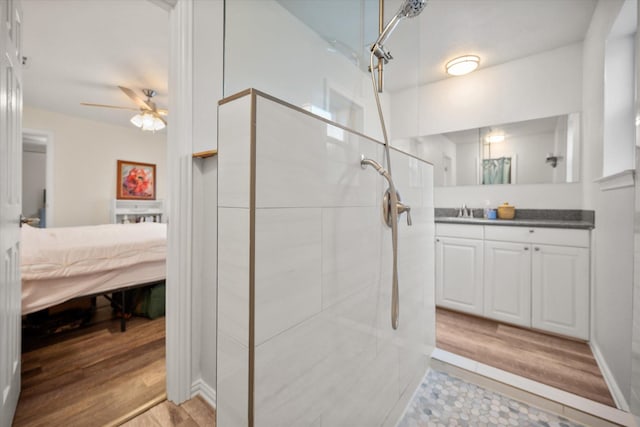 ensuite bathroom with wood finished floors, a tile shower, connected bathroom, and vanity