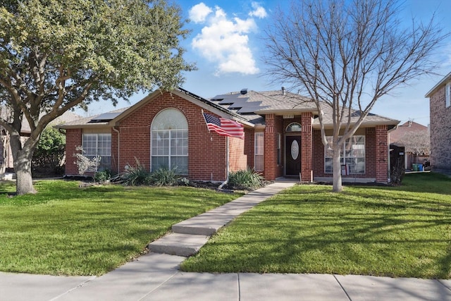 single story home featuring a front yard, brick siding, and solar panels