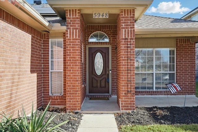 entrance to property featuring roof with shingles and brick siding