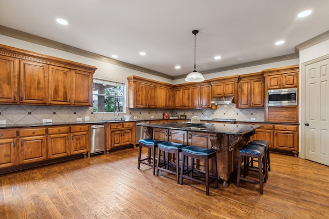 5805 Parker Village Dr, Parker, TX 75002 - kitchen with appliances with stainless steel finishes, under cabinet range hood, brown cabinetry, a kitchen breakfast bar, and dark wood finished floors