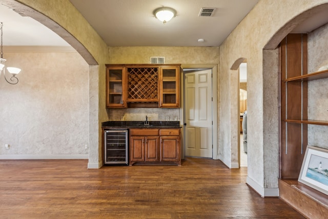 bar featuring dark wood-style floors, wine cooler, arched walkways, indoor wet bar, and visible vents