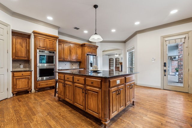5805 Parker Village Dr, Parker, TX 75002 - kitchen featuring appliances with stainless steel finishes, brown cabinetry, wood finished floors, tasteful backsplash, and crown molding