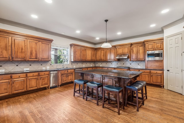 kitchen with a kitchen breakfast bar, appliances with stainless steel finishes, brown cabinets, and under cabinet range hood