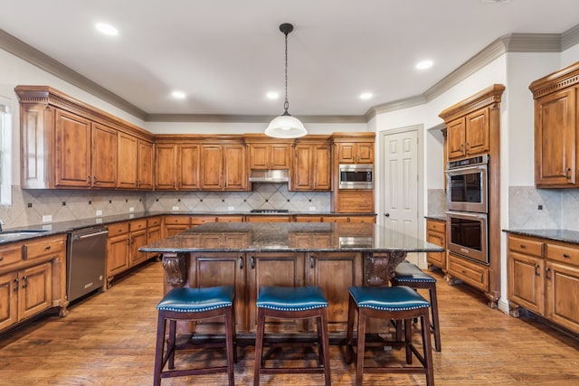 kitchen with brown cabinets, appliances with stainless steel finishes, a kitchen island, wood finished floors, and under cabinet range hood