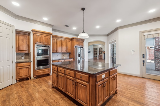 kitchen featuring arched walkways, pendant lighting, stainless steel appliances, light wood-style flooring, and brown cabinetry