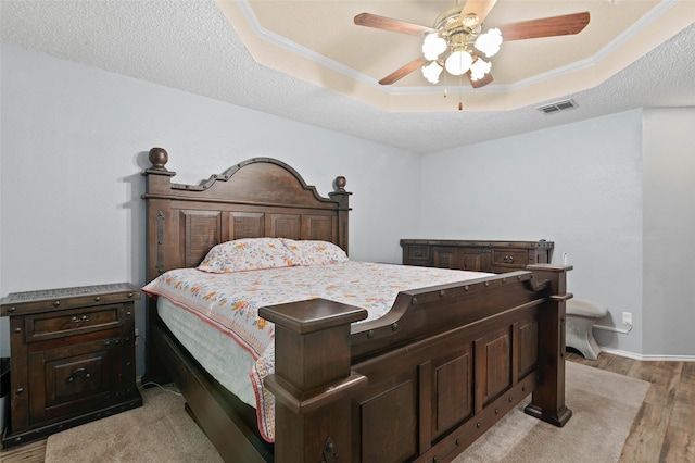 bedroom with light wood finished floors, visible vents, a raised ceiling, and crown molding