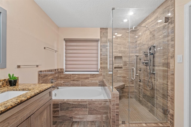 bathroom featuring a textured ceiling, a stall shower, a garden tub, and vanity