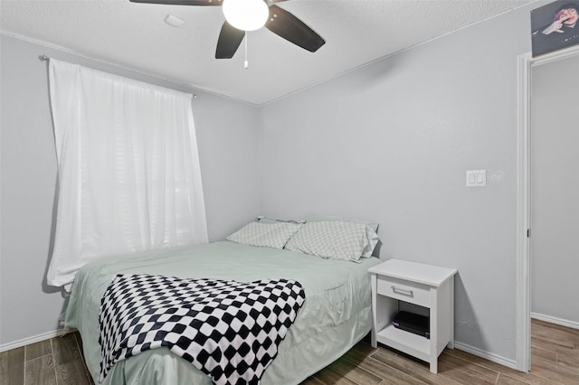 bedroom featuring ceiling fan, wood finish floors, a textured ceiling, and baseboards