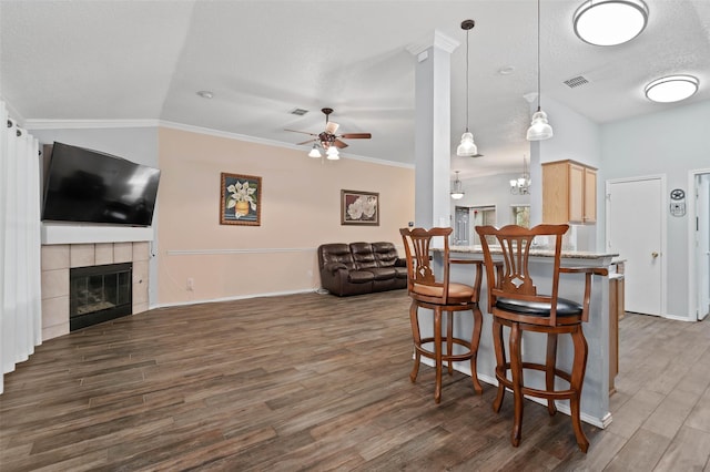 kitchen featuring a breakfast bar area, visible vents, open floor plan, a tiled fireplace, and dark wood finished floors