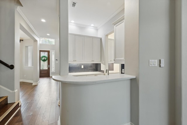 kitchen with decorative backsplash, wood finished floors, light countertops, crown molding, and white cabinetry