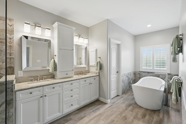 full bathroom featuring double vanity, wood finished floors, a soaking tub, and a sink