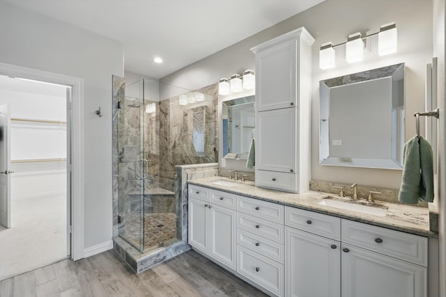 bathroom with double vanity, a stall shower, a sink, and wood finished floors