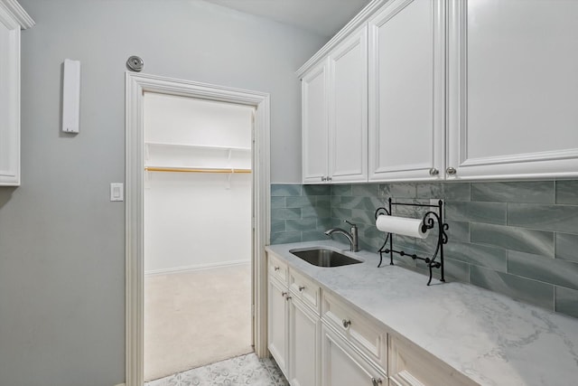 interior space featuring baseboards, a sink, light stone countertops, white cabinetry, and backsplash