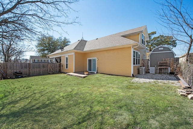 rear view of house with a storage unit, a fenced backyard, a yard, an outdoor structure, and a shingled roof