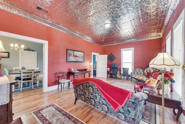 living room with wood finished floors, visible vents, an ornate ceiling, crown molding, and a notable chandelier