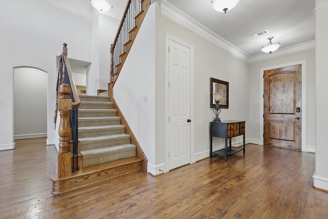 entrance foyer with visible vents, crown molding, baseboards, wood finished floors, and arched walkways