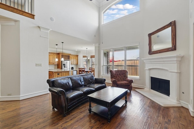 living area featuring a fireplace with raised hearth, dark wood-type flooring, baseboards, and a towering ceiling