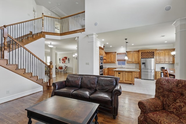 living area featuring baseboards, light wood-style floors, ornate columns, and ornamental molding