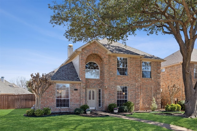 view of front of home with brick siding, roof with shingles, a front yard, and fence