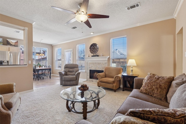 living room with a tile fireplace, visible vents, a ceiling fan, and ornamental molding