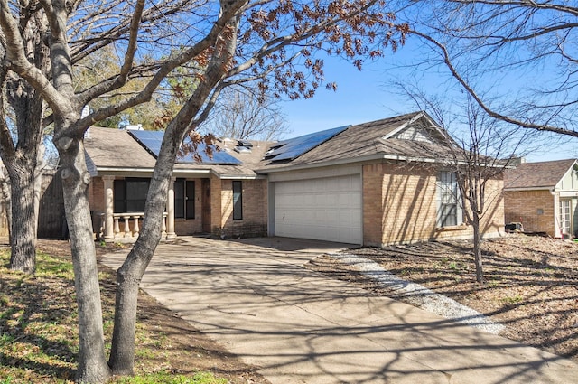 ranch-style home with a garage, concrete driveway, brick siding, and roof mounted solar panels