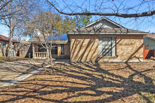 back of house featuring a porch, roof mounted solar panels, brick siding, and driveway