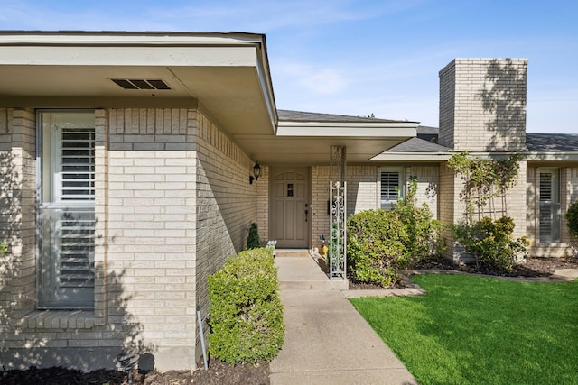 property entrance with a chimney, brick siding, a yard, and visible vents