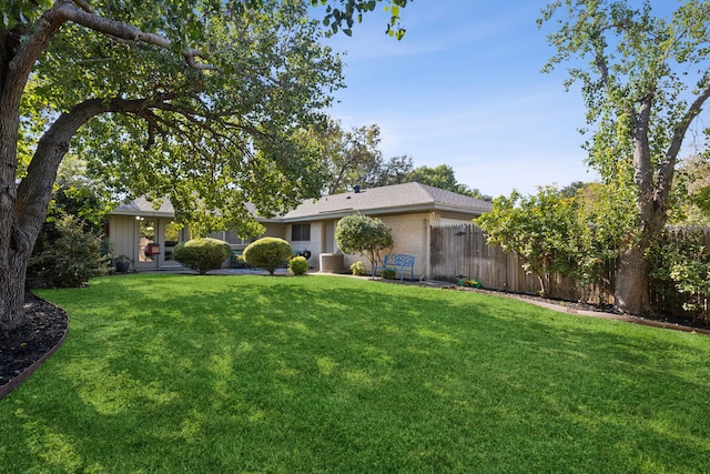 ranch-style home featuring central AC unit, a shingled roof, fence, a front yard, and brick siding