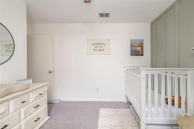 bedroom with light colored carpet, visible vents, ceiling fan, a crib, and baseboards