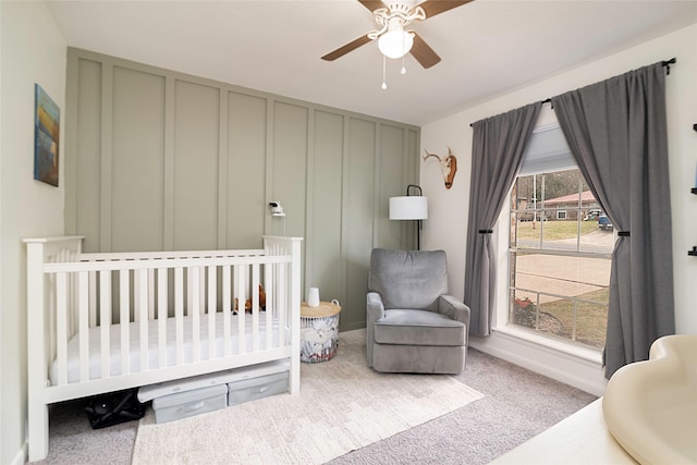 bedroom featuring carpet floors, a nursery area, a decorative wall, and ceiling fan