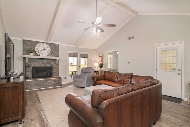 living area with a stone fireplace, visible vents, a ceiling fan, light wood-type flooring, and beam ceiling