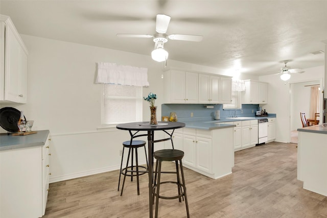 kitchen with light wood-style flooring, a ceiling fan, white cabinets, white dishwasher, and a peninsula