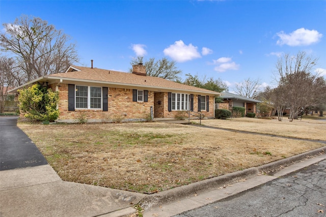 ranch-style home featuring roof with shingles, brick siding, a chimney, and a front lawn