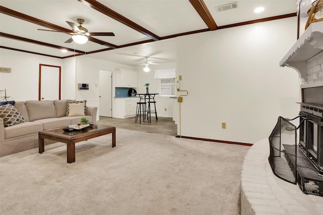 living area featuring beam ceiling, visible vents, a fireplace with raised hearth, light carpet, and baseboards