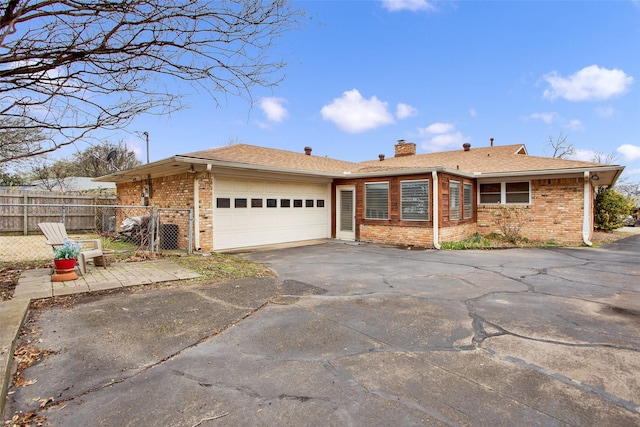 ranch-style home featuring an attached garage, fence, aphalt driveway, and brick siding